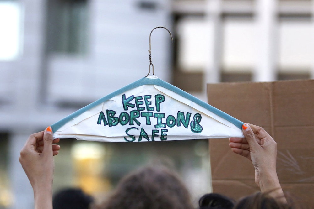 A photograph of a protester holding up a wire hanger with the words "keep abortion safe" written on it to illustrate this story.