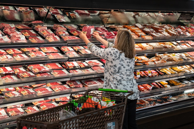A shopper reaches for a package of meat in a supermarket.