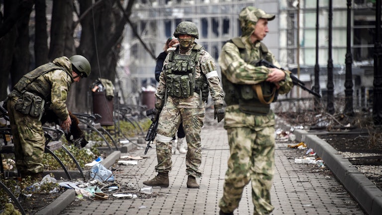 Three soldiers carry guns in a street littered with detritus.