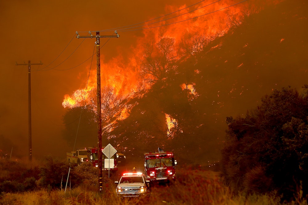 Emergency vehicles drive toward the camera with a fire in the background.