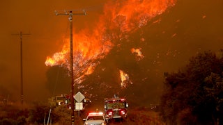 Emergency vehicles drive toward the camera with a fire in the background.