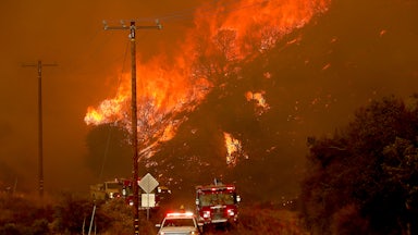 Emergency vehicles drive toward the camera with a fire in the background.