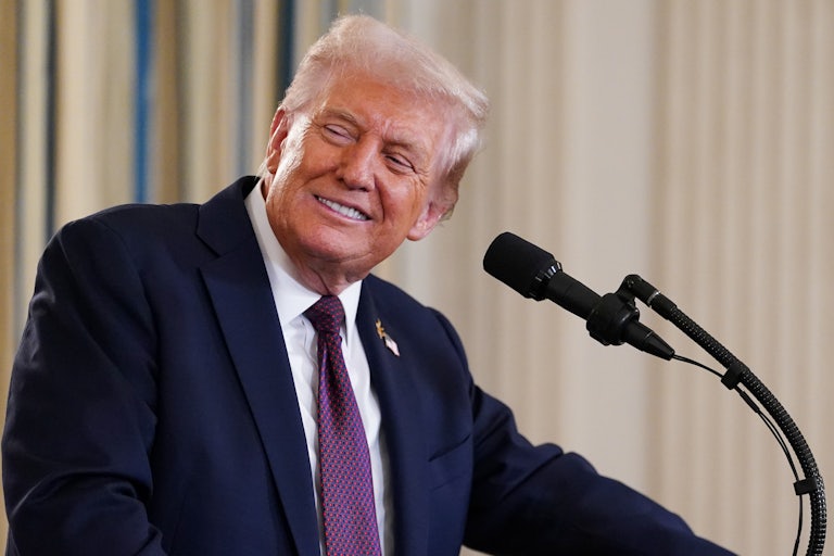 Donald Trump smiles and turns to the side while standing at a microphone