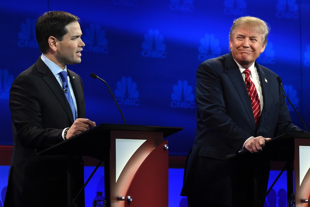 Donald Trump smiles as he stands behind a lectern and looks over at Marco Rubio, who is talking.