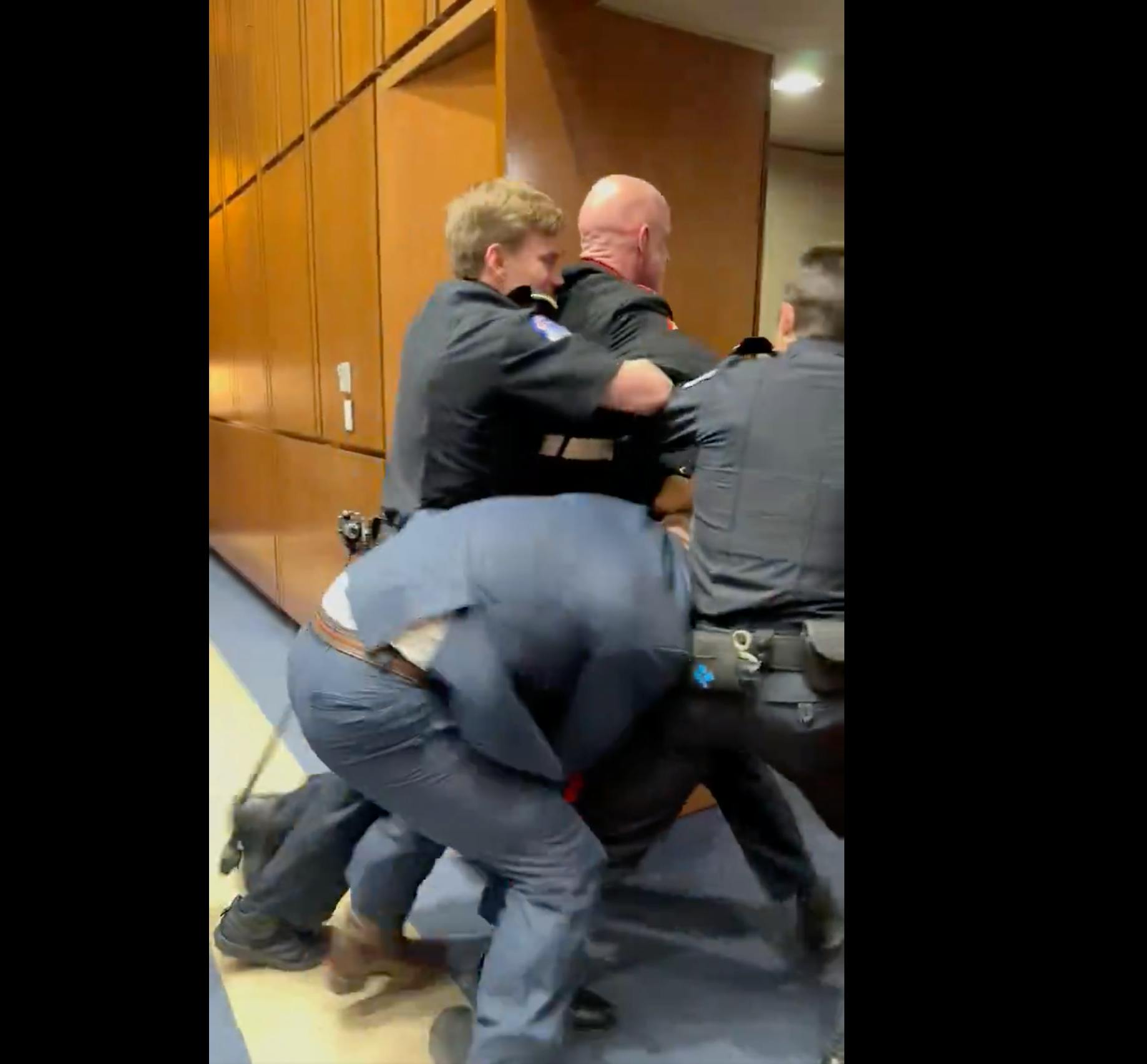 Two police officers and Senator Tim Sheehy all try to force Marine veteran Brian McGinnis out of a doorway.