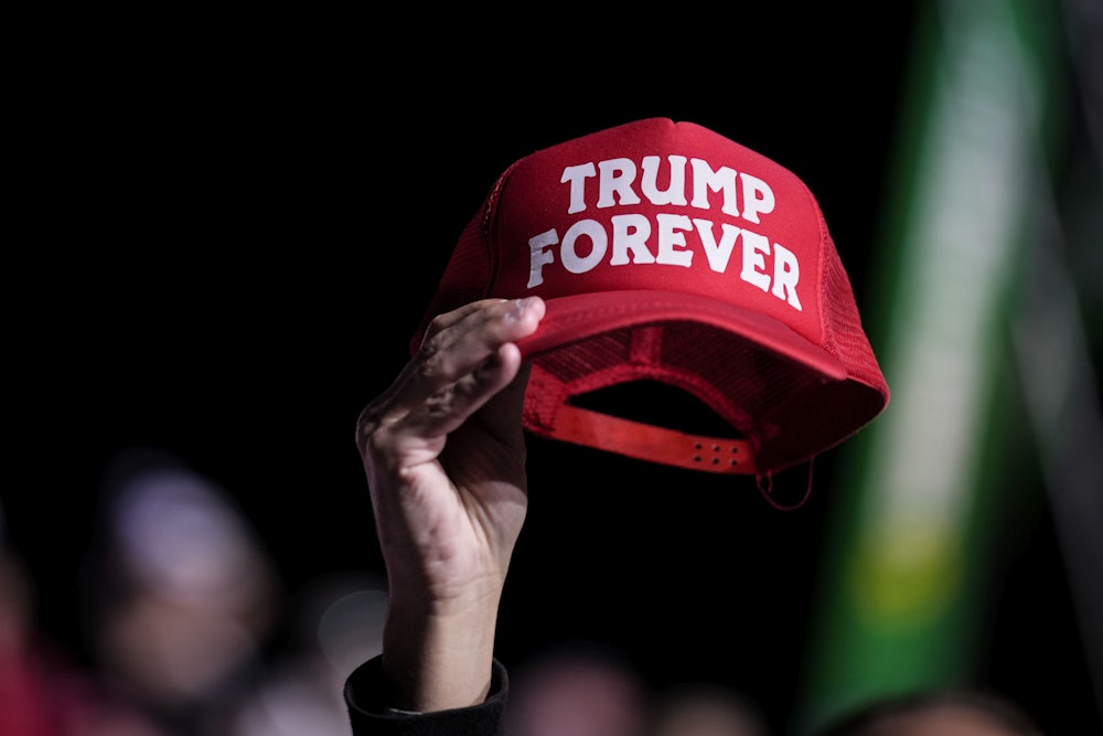 A hand holds a red hat reading "TRUMP FOREVER."