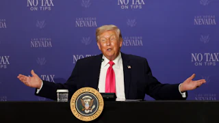 Donald Trump holds his arms out to the side while sitting at a table