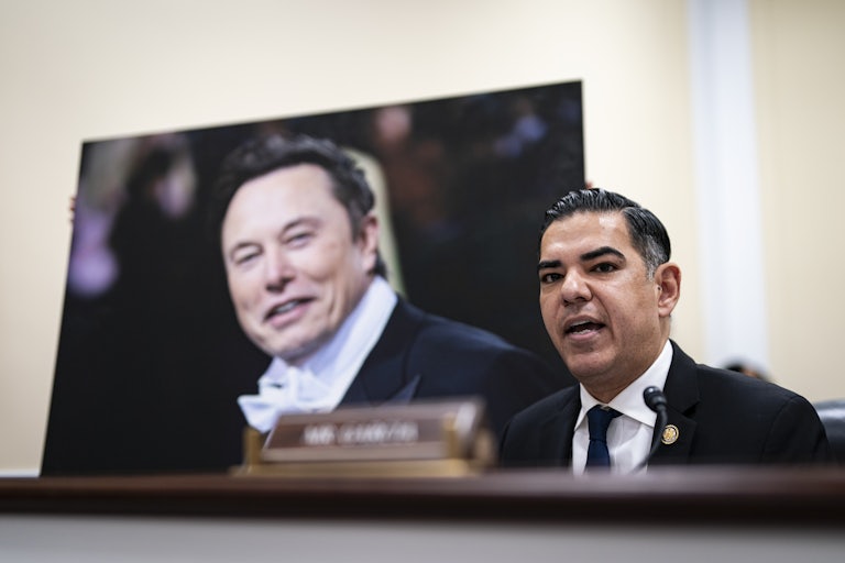 Representative Robert Garcia speaks during a congressional hearing, with a big photo of Elon Musk behind him.