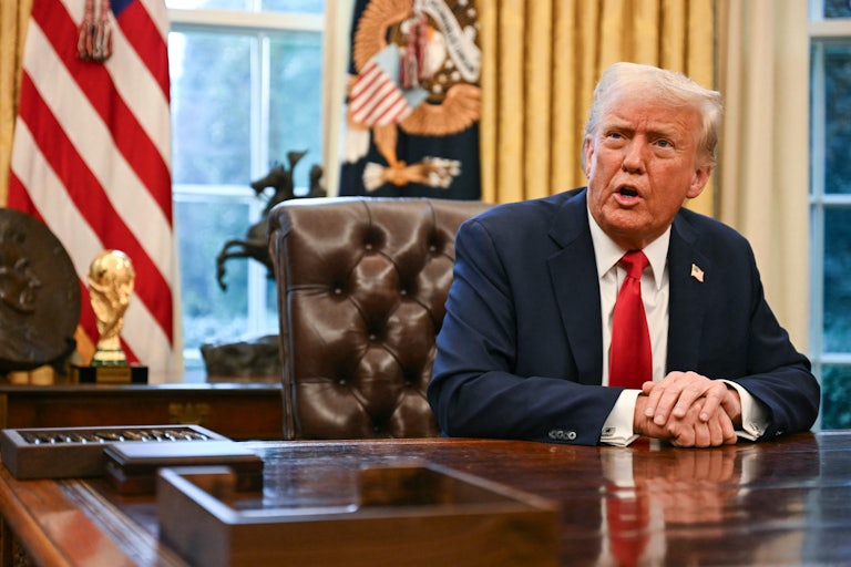 Donald Trump sits with his hands folded on his desk while speaking to reporters in the Oval Office