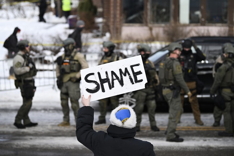 A person holds up a sign that says, "Shame" while standing across from federal agents in Minneapolis, Minnesota
