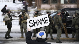 A person holds up a sign that says, "Shame" while standing across from federal agents in Minneapolis, Minnesota