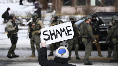 A person holds up a sign that says, "Shame" while standing across from federal agents in Minneapolis, Minnesota
