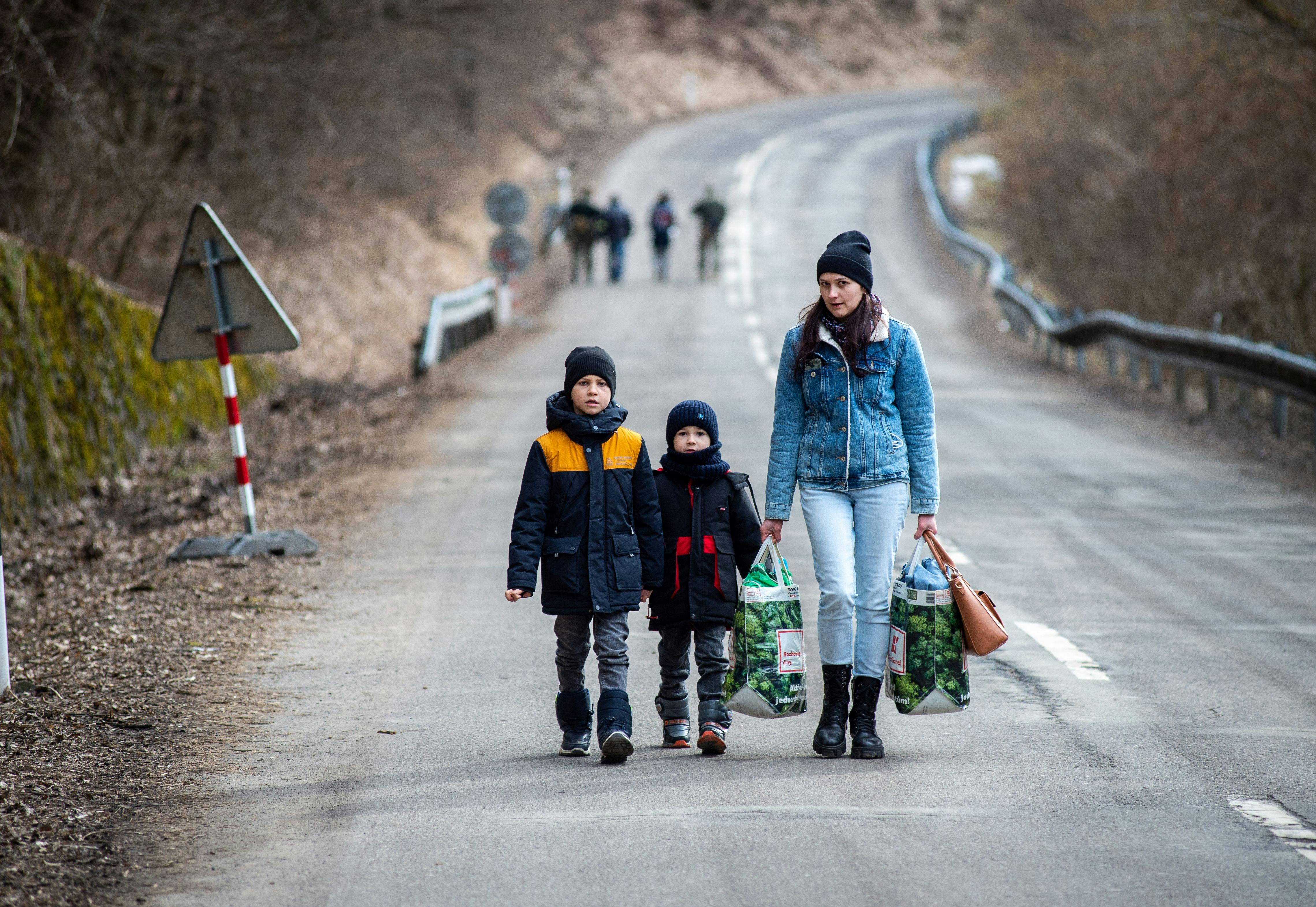 A woman with two children and carrying bags walk on a street to leave Ukraine after crossing the Slovak-Ukrainian border.