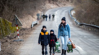 A woman with two children and carrying bags walk on a street to leave Ukraine after crossing the Slovak-Ukrainian border.