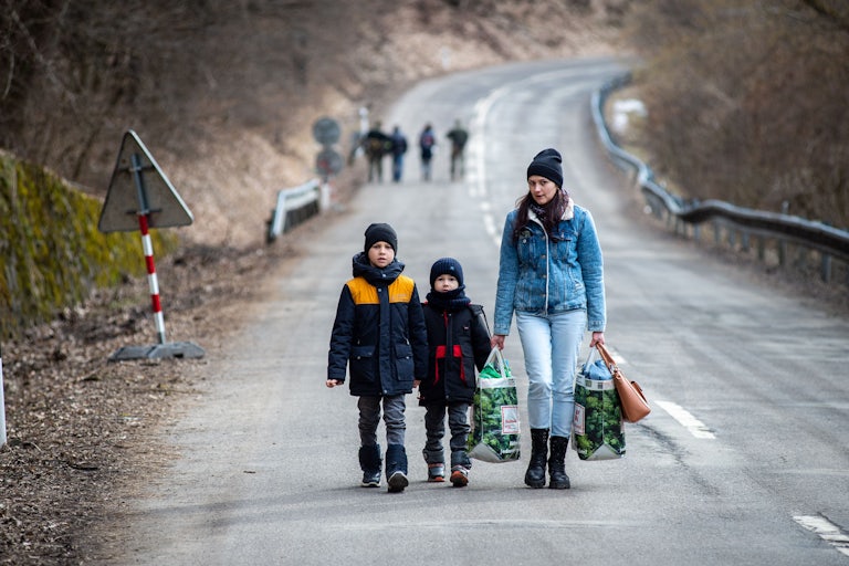 A woman with two children and carrying bags walk on a street to leave Ukraine after crossing the Slovak-Ukrainian border.