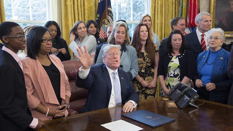 Former President Trump, surrounded by supporters in the Oval Office, signs an anti-sex trafficking bill