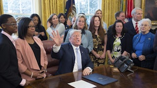 Former President Trump, surrounded by supporters in the Oval Office, signs an anti-sex trafficking bill
