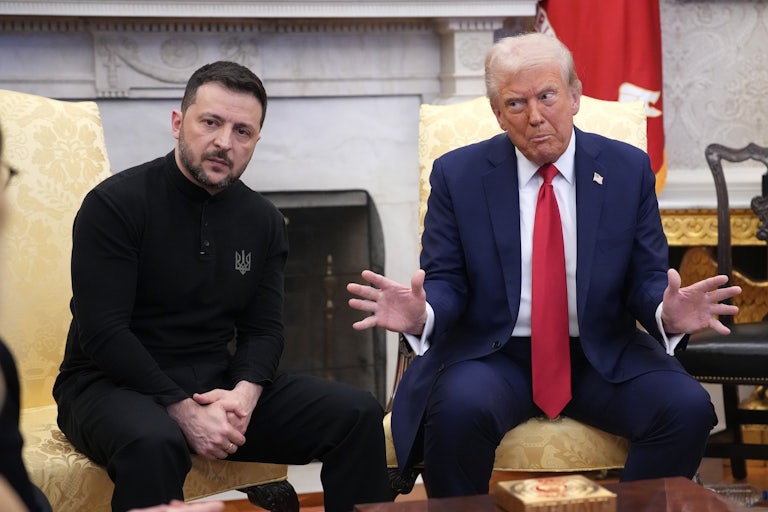 Ukranian Presideny Volodymr Zelenskiy and Donald Trump are seated in the White House. Zelenskiy clasps his hands and listens earnestly while looking at soemeone off camera. Trump glares at him and splays both hands outward.