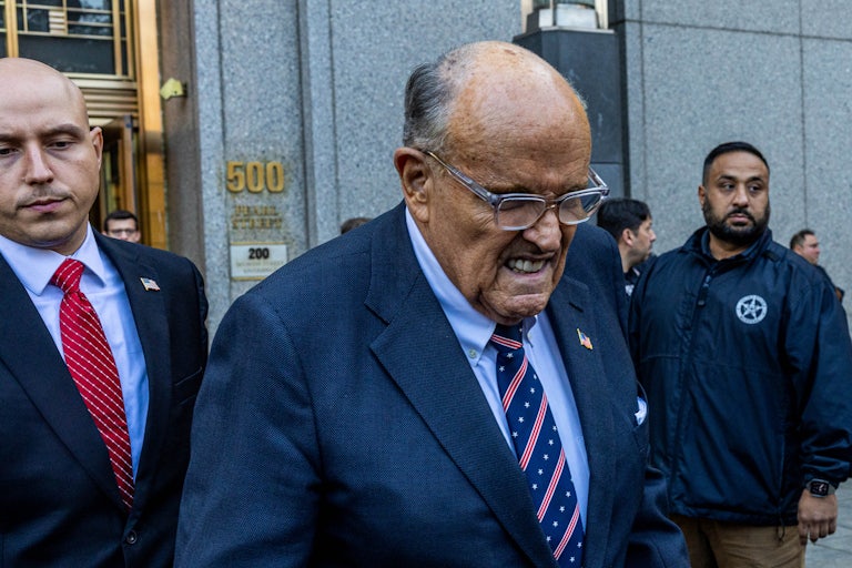 Rudy Giuliani frowns and looks down while walking