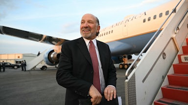 Commerce Secretary Howard Lutnick holds a folder and smiles as he boards Air Force One.