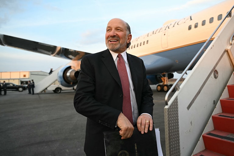 Commerce Secretary Howard Lutnick holds a folder and smiles as he boards Air Force One.