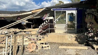 A partially collapsed roof hangs over debris from a damaged building.