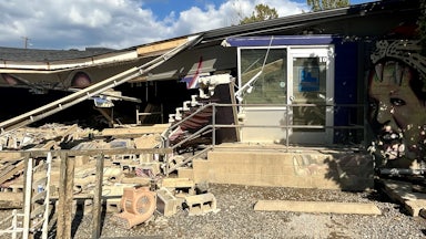 A partially collapsed roof hangs over debris from a damaged building.