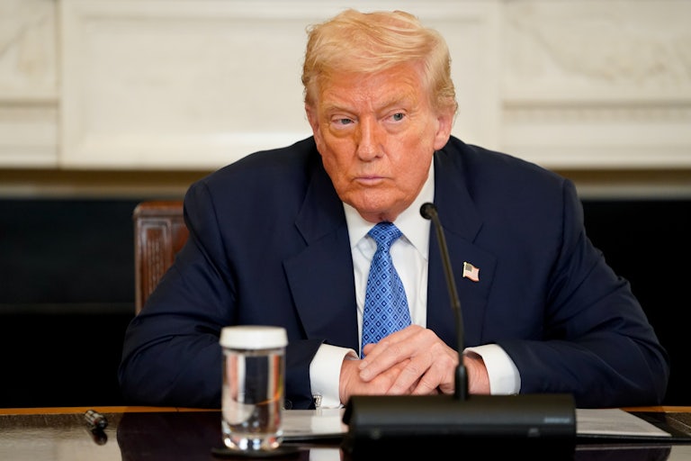 Donald Trump sits with a mic and a glass of water on the table in front of him.