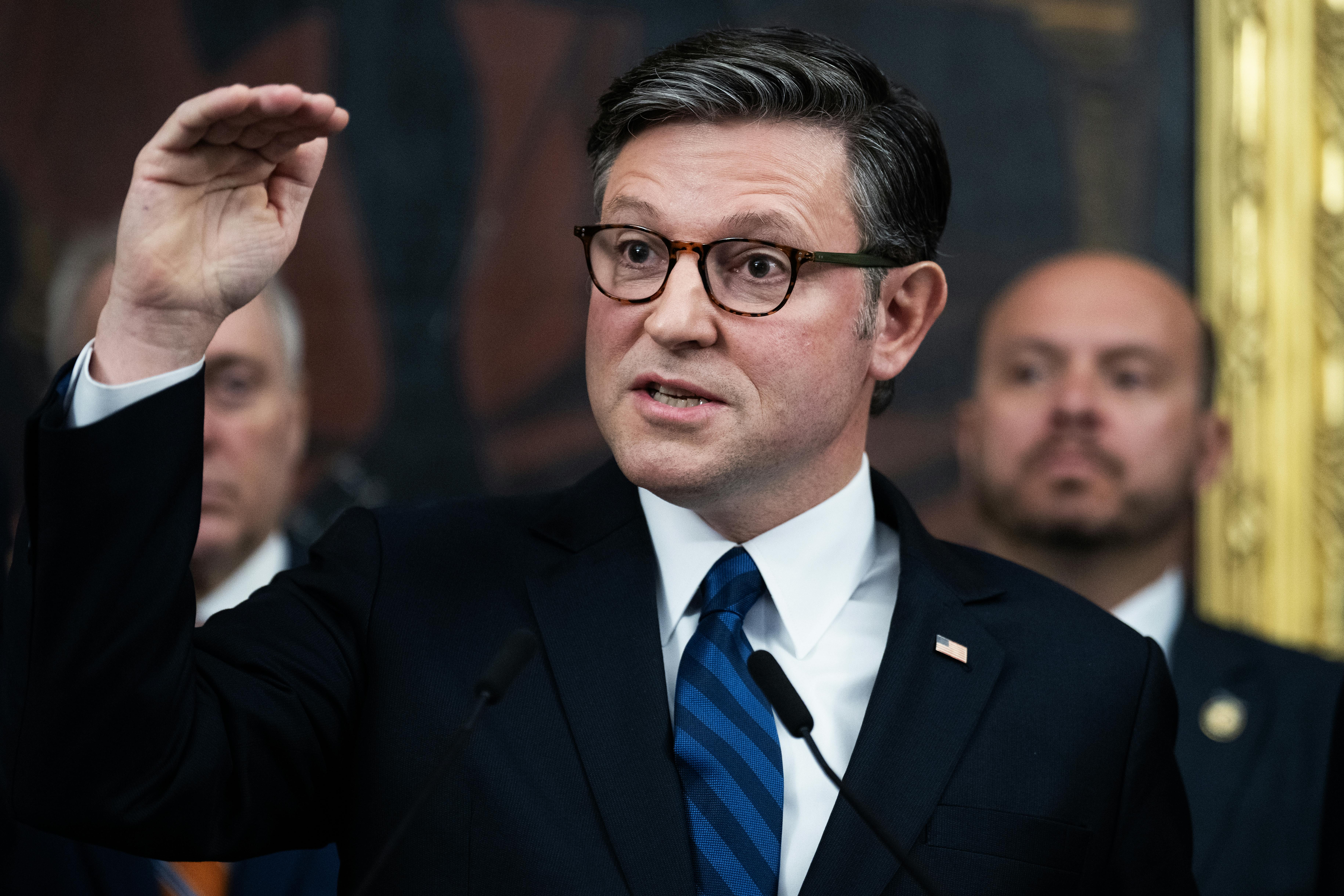 House Speaker Mike Johnson holds his hand horizontally above his head while speaking during a press conference