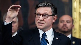 House Speaker Mike Johnson holds his hand horizontally above his head while speaking during a press conference