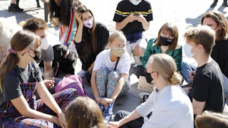 Young people sit, wearing facemasks, on the ground.