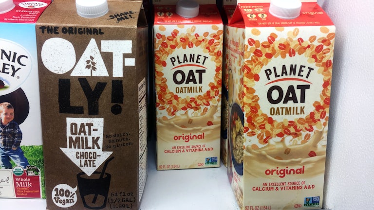 Oatly and Planet Oat oat milk stand on a supermarket shelf.