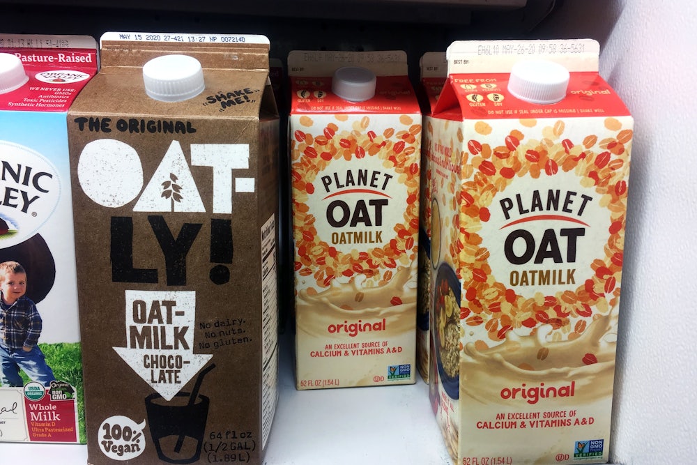 Oatly and Planet Oat oat milk stand on a supermarket shelf.