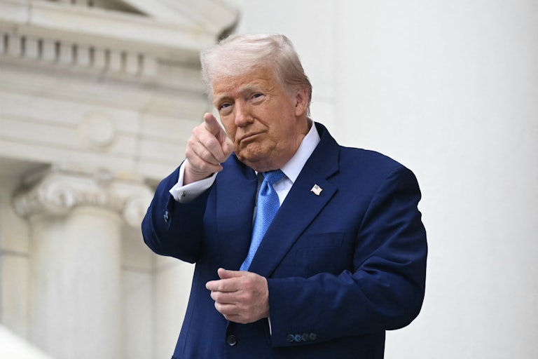 Donald Trump smiles and points to something in the distance.