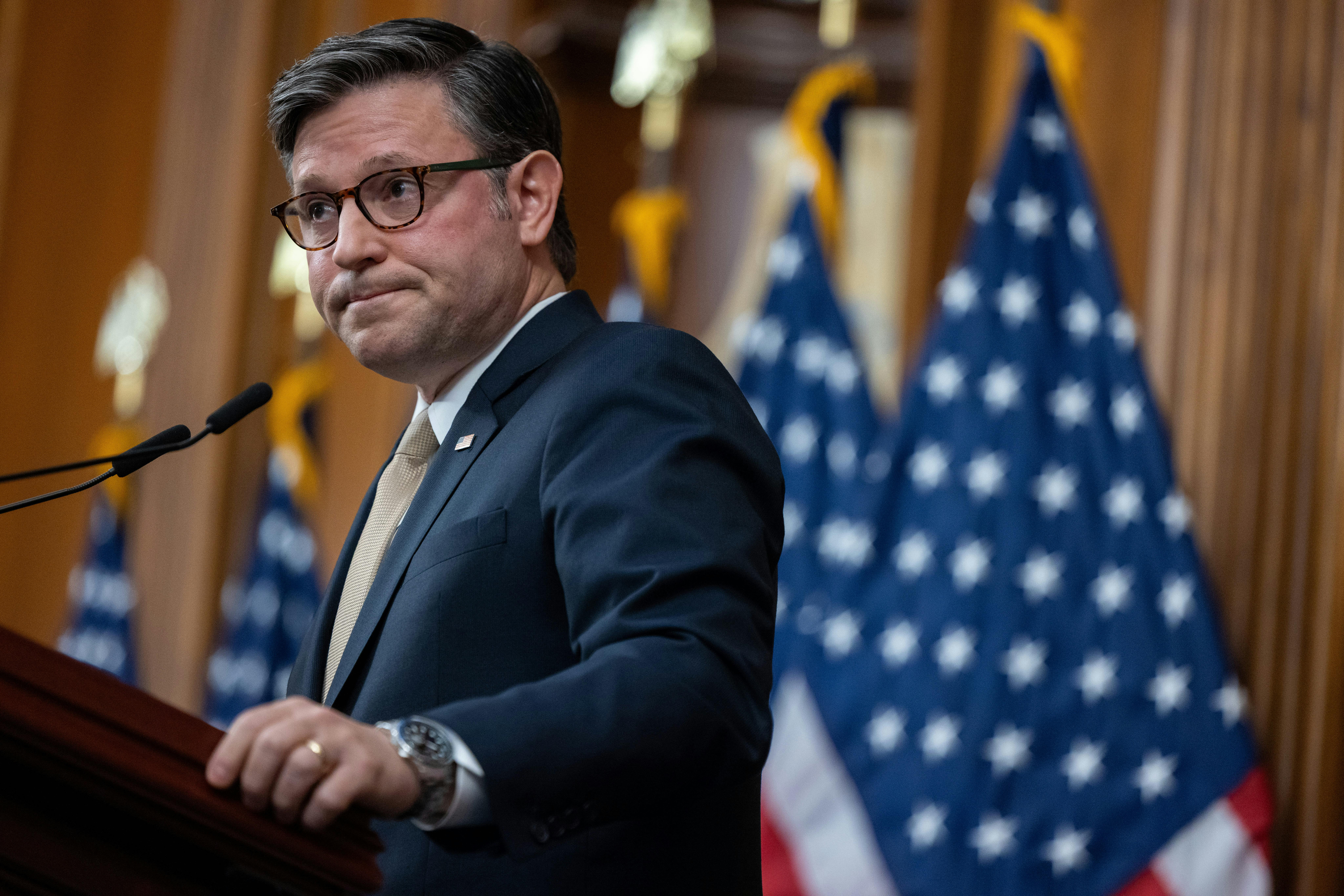 House Speaker Mike Johnson frowns while standing at a podium