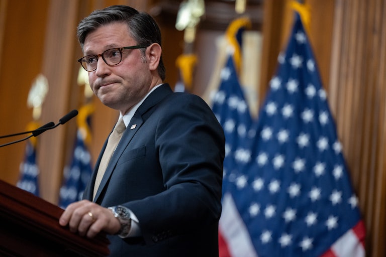 House Speaker Mike Johnson frowns while standing at a podium