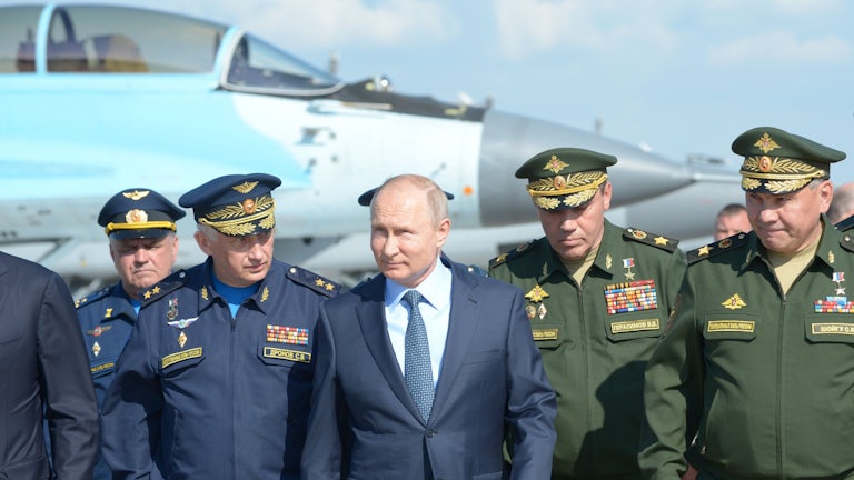 Russian President Vladimir Putin, surrounded by top military officers and officials, tours a military flight test center.