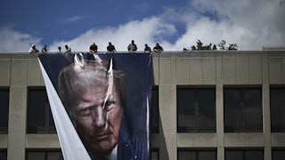 Workers hang a large banner of Donald Trump's face from the roof of the Department of Labor headquarters building.