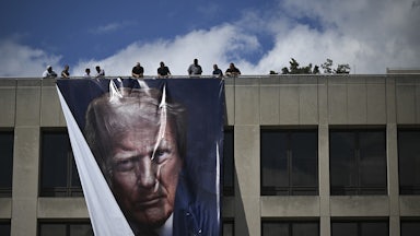 Workers hang a large banner of Donald Trump's face from the roof of the Department of Labor headquarters building.