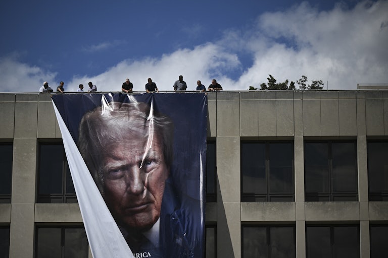 Workers hang a large banner of Donald Trump's face from the roof of the Department of Labor headquarters building.