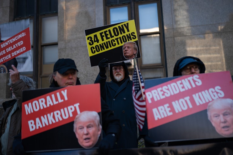 People hold protest signs against Donald Trump outside the Manhattan courthouse