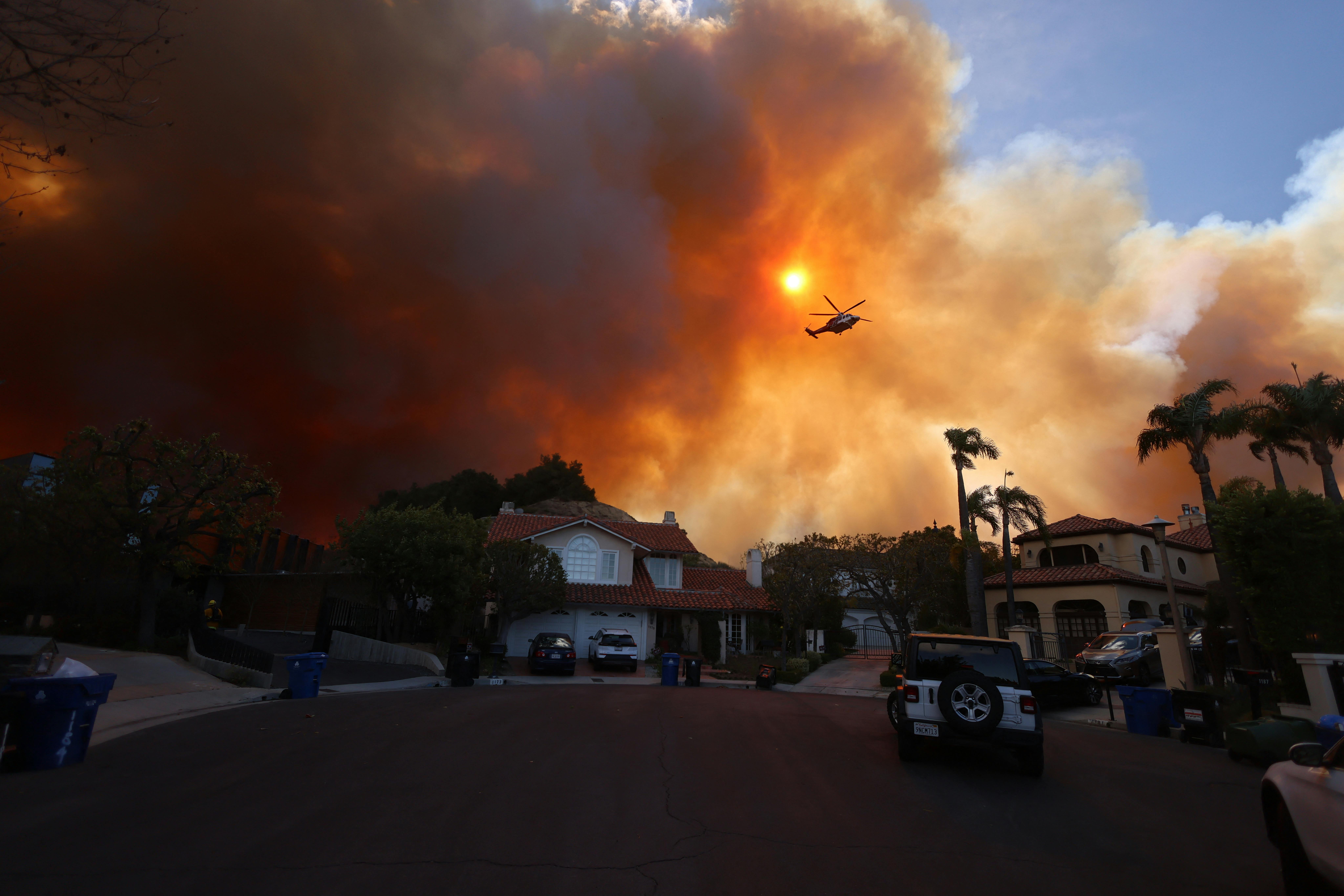Plumes of smoke billow over a cul-de-sac with large houses.