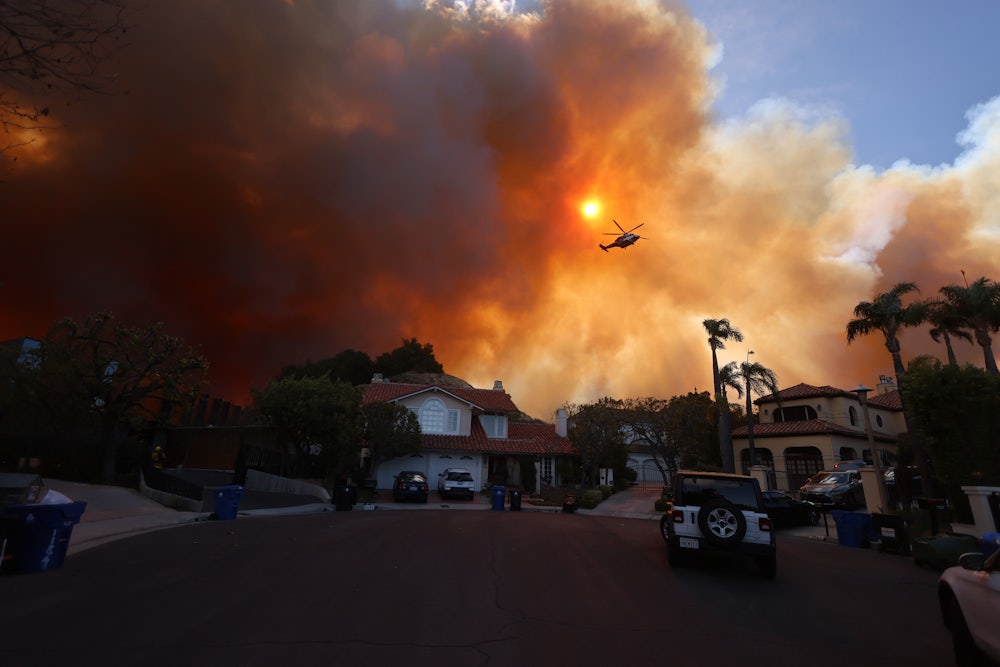 Plumes of smoke billow over a cul-de-sac with large houses.