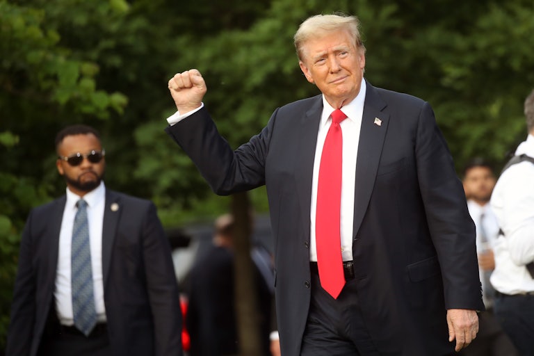 Donald Trump holds up a fist while campaigning in 2024. A Black security guard stands behind him.