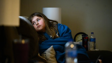 A child sits in a chair, looking off to the side.