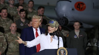 Donald Trump stands behind Gretchen Whitmer as she gestures and speaks onstage at one of his events