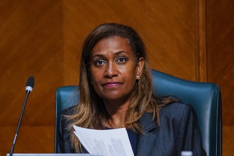 Letitia Plummer holds a stack of papers and is seated before a mic during a city coucnil meeting