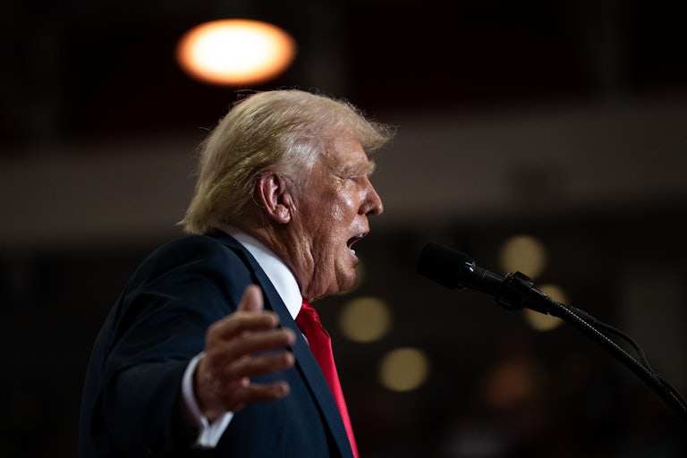 Donald Trump holds his arms out while speaking into a microphone at a rally