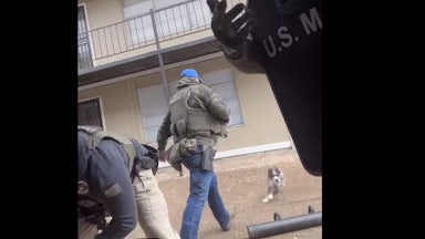 A screenshot of a U.S. Marshal approaching the dog before kicking it.