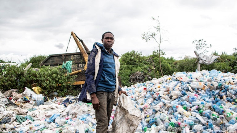 A man holding a bag stands in front of a large mound of plastic trash.